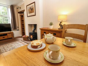 A cozy living room with a fireplace, a television, a dining table with a cake and teapot, and a lamp. - 27 Bongate (Appleby-in-Westmorland)