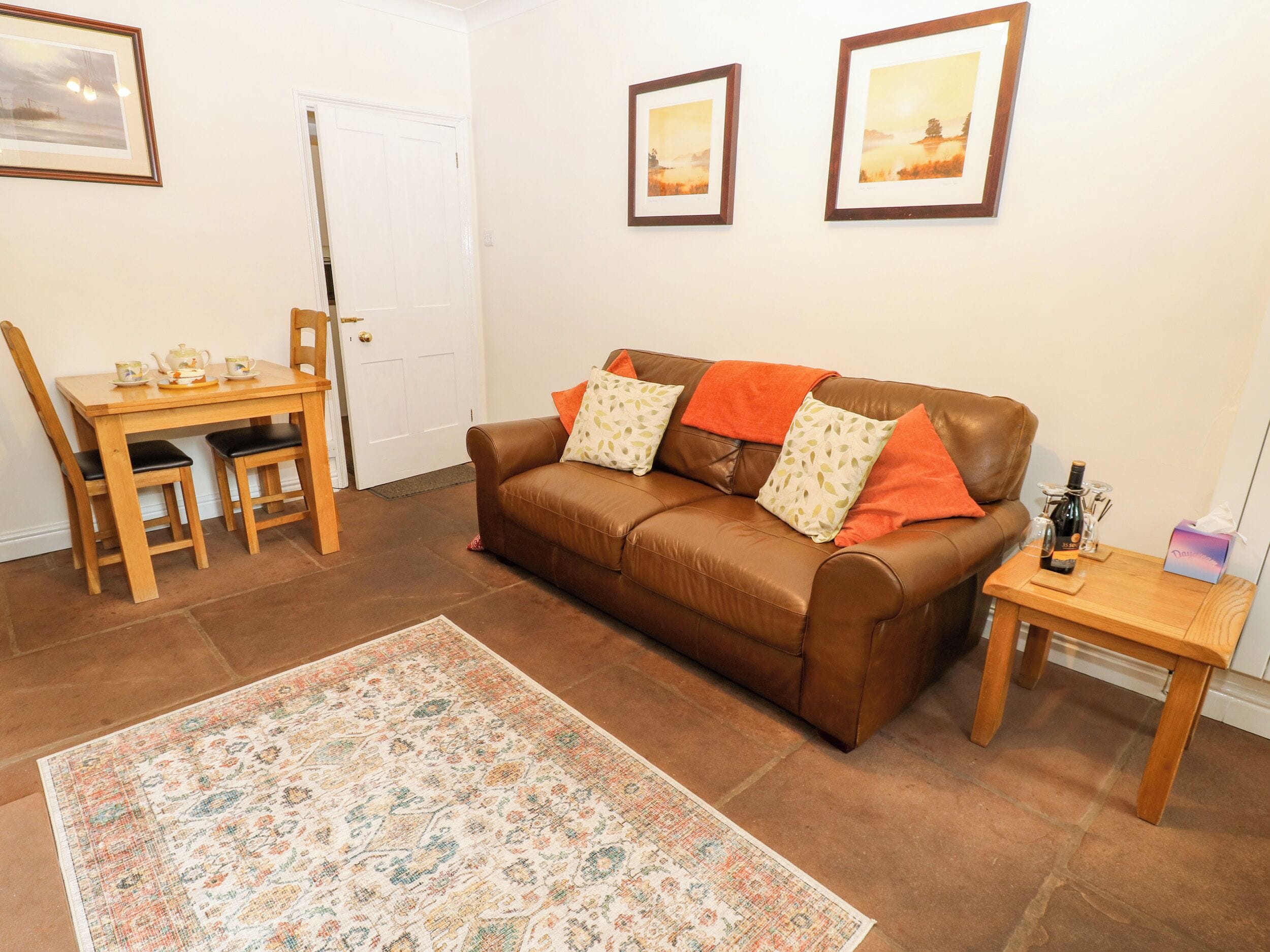 A living room with a brown leather sofa, a wooden coffee table, a patterned rug, and framed pictures on the wall.