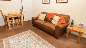 A living room with a brown leather sofa, a wooden coffee table, a patterned rug, and framed pictures on the wall. - 27 Bongate (Appleby-in-Westmorland)