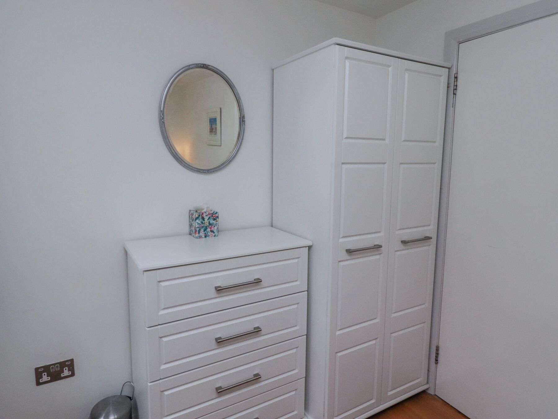 A white wardrobe with multiple doors and drawers, a small mirror above it, and a tissue box on the lower shelf.
