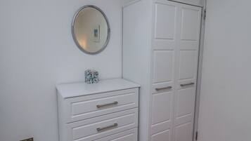 A white wardrobe with multiple doors and drawers, a small mirror above it, and a tissue box on the lower shelf.