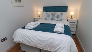 A neatly made bed with white linens and a teal throw, two bedside lamps, and a framed picture on the wall. - 6 Mill Wharf (Berwick-upon-Tweed)
