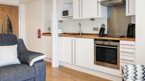 A compact kitchen with white cabinets, a microwave, a stove, and a coffee maker. - 6 Mill Wharf (Berwick-upon-Tweed)