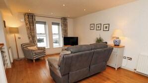A modern living room with a grey sofa, patterned armchair, and a television on a stand. - 6 Mill Wharf (Berwick-upon-Tweed)