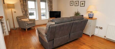 A modern living room with a grey sofa, patterned armchair, and a television on a stand.