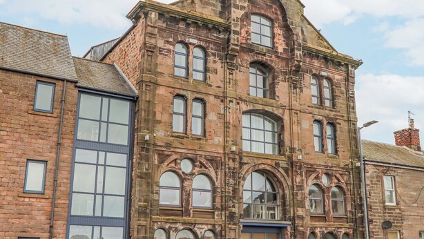 A historic building with multiple windows, a prominent arched entrance, and a brick facade. - 6 Mill Wharf (Berwick-upon-Tweed)