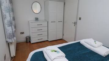 A bedroom with a bed, two white towels, a blue blanket, a white wardrobe, a mirror, and a radiator.