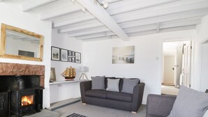 A living room with a fireplace, a grey sofa, a mirror, framed pictures, and a painting on the wall. - Marsh Villa (Wigton)