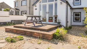 A two-story house with a patio area featuring a wooden table and benches. - Marsh Villa (Wigton)