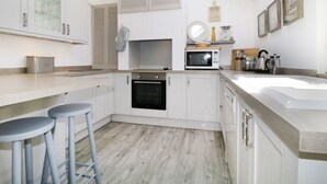 A modern kitchen with white cabinets, a microwave, an oven, and a skylight. - Marsh Villa (Wigton)