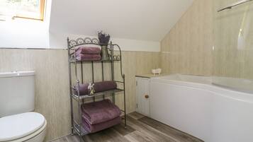 A bathroom with a white toilet, a metal towel rack with folded towels, a small vase with flowers, and a white bathtub.