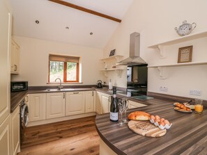 A modern kitchen with wooden flooring, a built-in oven, a stainless steel range hood, and a window with a view of trees. - Pentre Fach (Llandrindod Wells)