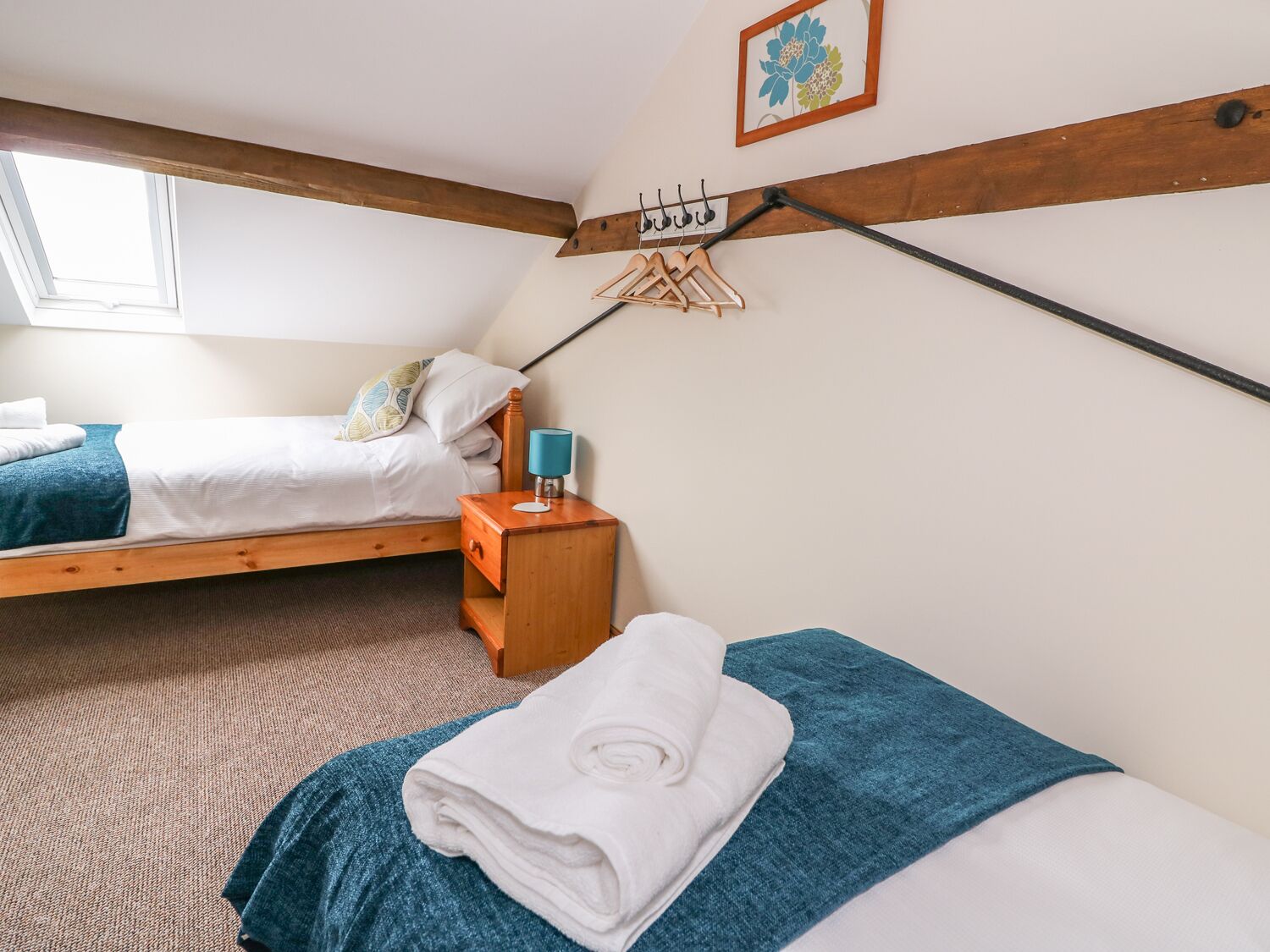 A bedroom with two beds, a wooden headboard, a nightstand, a lamp, and a window.