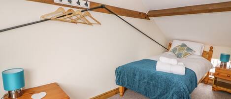 Un dormitorio con cama, mesitas de noche de madera, perchero y un cuadro en la pared, además de una lámpara azul.