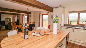 A spacious kitchen with a wooden island, a dining area with a table and chairs, and a view of the outdoors through a window. - Pentre Fawr (Llandrindod Wells)
