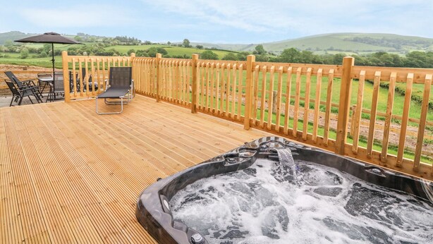 A wooden deck with a hot tub, outdoor furniture, and a view of green hills. - Pentre Fawr (Llandrindod Wells)