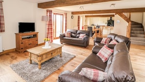 A cozy living room with a wooden ceiling, a television on a wooden stand, a brown leather sofa, and a dining area in the background. - Pentre Fawr (Llandrindod Wells)