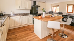 A modern kitchen with a central island, wooden flooring, and a built-in washing machine. - Pentre Fawr (Llandrindod Wells)
