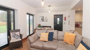 Una sala de estar con un sofá, una silla y una mesa de comedor. Se ve una puerta y una ventana con persianas.