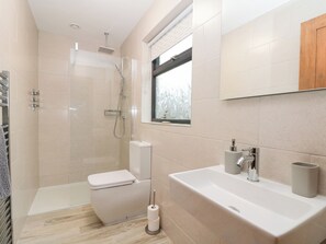 A modern bathroom with a glass-enclosed shower, a toilet, a sink, and a window. - Fieldside (Filey)
