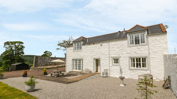 A two-story stone house with a gravel driveway and outdoor seating area. - Bracken Holiday Cottage (Dalbeattie)