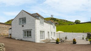 A white stone house with a paved driveway and outdoor seating area. - Bracken Holiday Cottage (Dalbeattie)