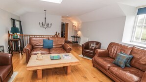 A spacious living room with a wooden coffee table, leather sofas, and a chandelier. - Bracken Holiday Cottage (Dalbeattie)