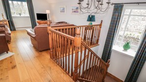 A spacious living room with a wooden staircase, a sofa, a television, and a view of the outdoors. - Bracken Holiday Cottage (Dalbeattie)