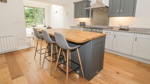 A modern kitchen with a central island, grey cabinets, and a stainless steel range hood. - Oak Cottage (Barnard Castle)