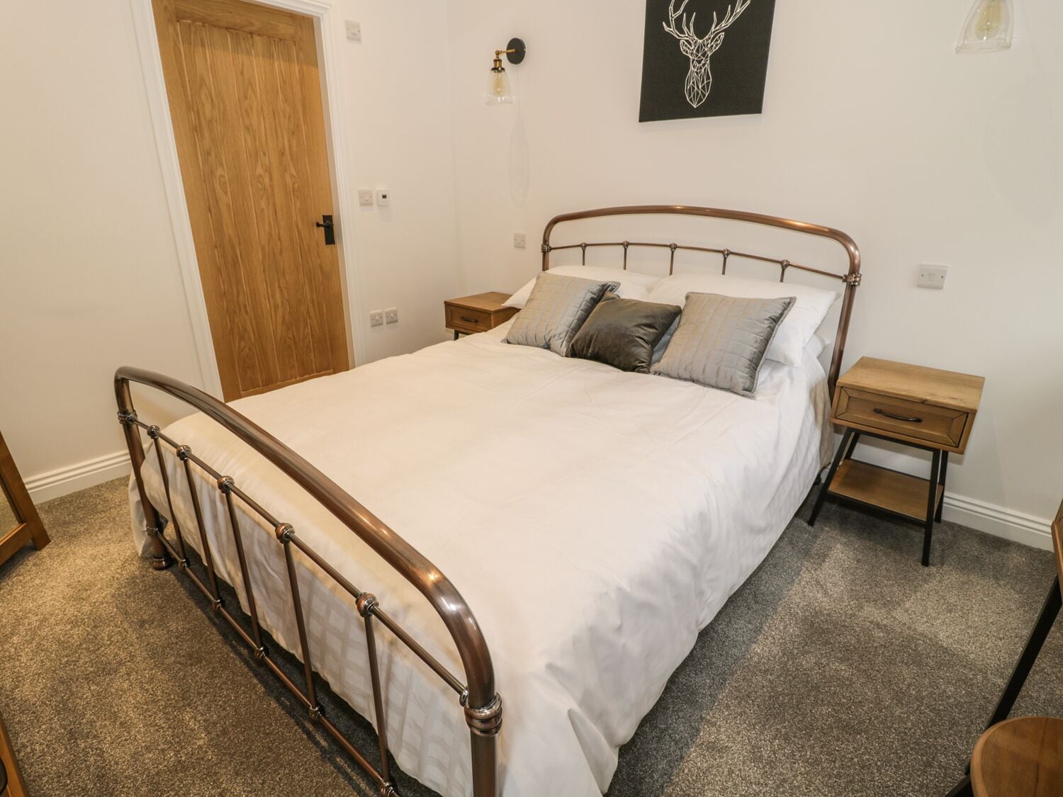 Ein ordentlich bezogenes Bett mit Metallgestell, zwei Nachttische und eine Holztür.