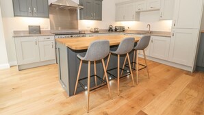 A modern kitchen with grey cabinets, a wooden island with bar stools, and stainless steel appliances. - Oak Cottage (Barnard Castle)