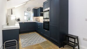 A modern kitchen with dark cabinetry, a built-in oven, and a small window. - Trefollwyn Mawr (Pwllheli)