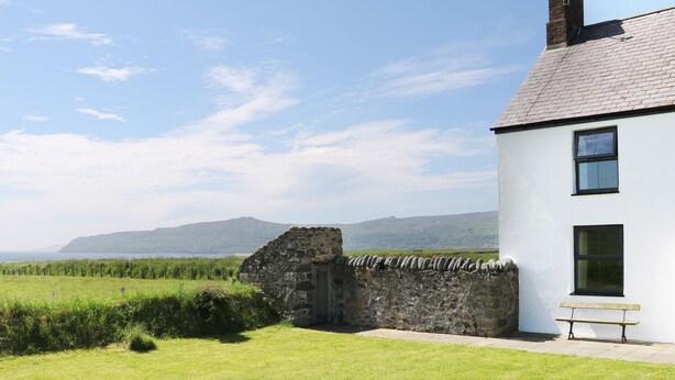 A white building with a stone wall and a bench outside. - Trefollwyn Mawr (Pwllheli)