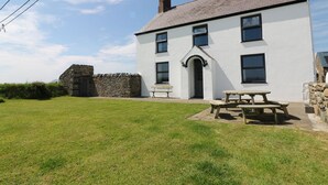 A white building with a stone wall, a wooden bench, and a picnic table in front. - Trefollwyn Mawr (Pwllheli)