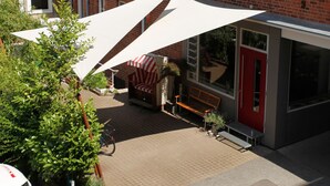 A courtyard with a brick building, a red door, and a white awning providing shade. - Hotel an der Marienkirche (Lübeck)