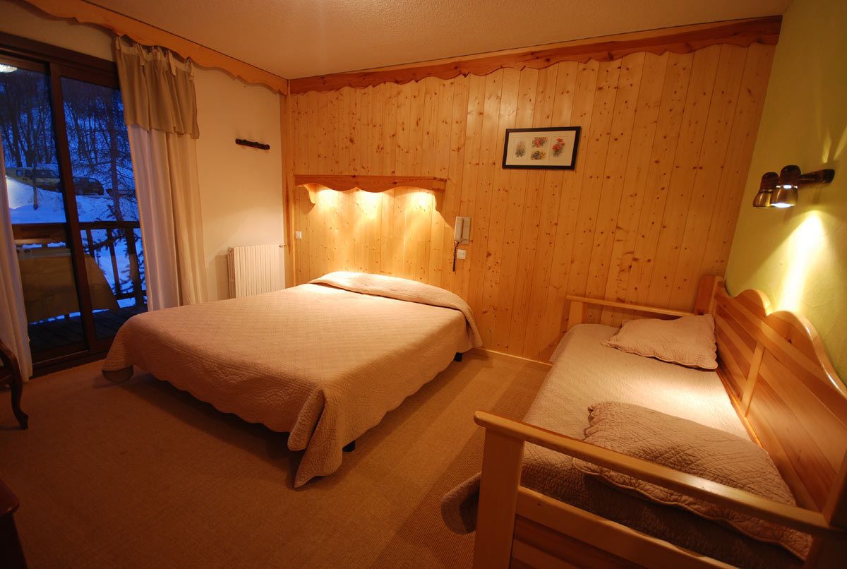 Une chambre avec deux lits, une tête de lit en bois, un tableau encadré et une fenêtre avec des rideaux.