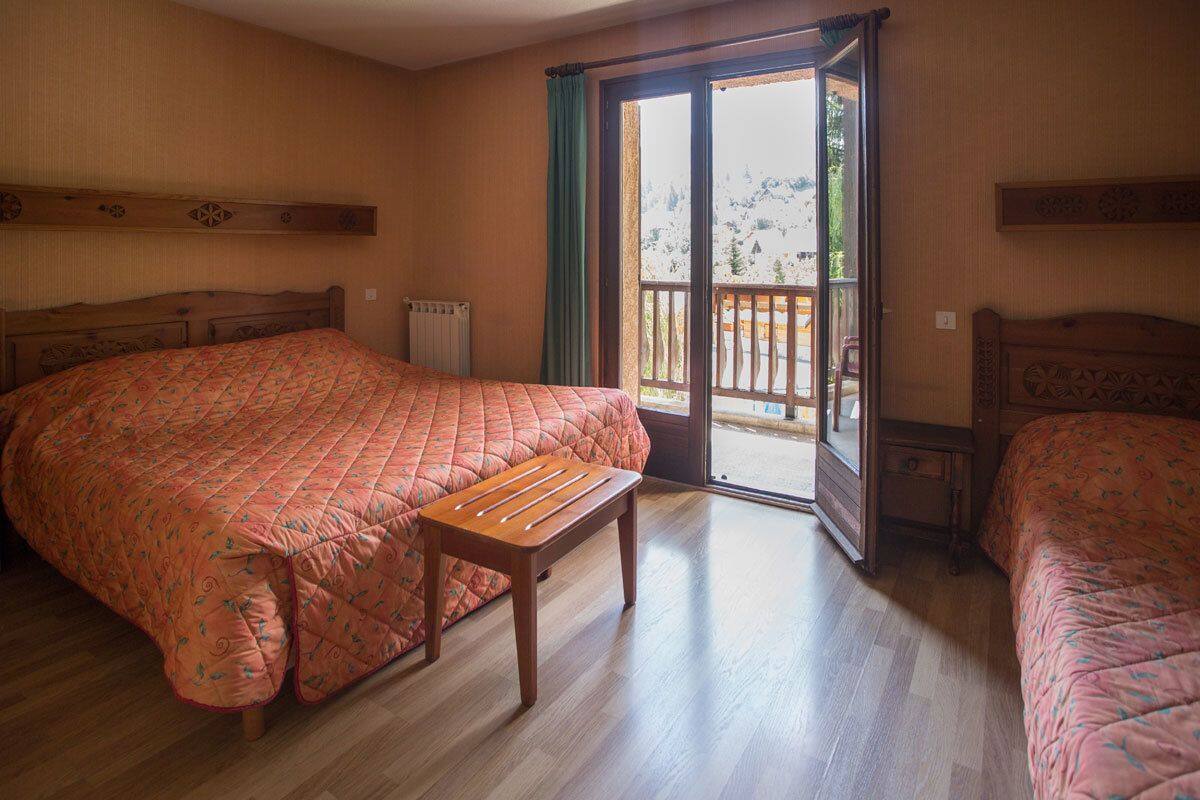 Un dormitorio con una cama grande, una cama más pequeña, un banco de madera y un ventanal corredera que da a un espacio al aire libre.