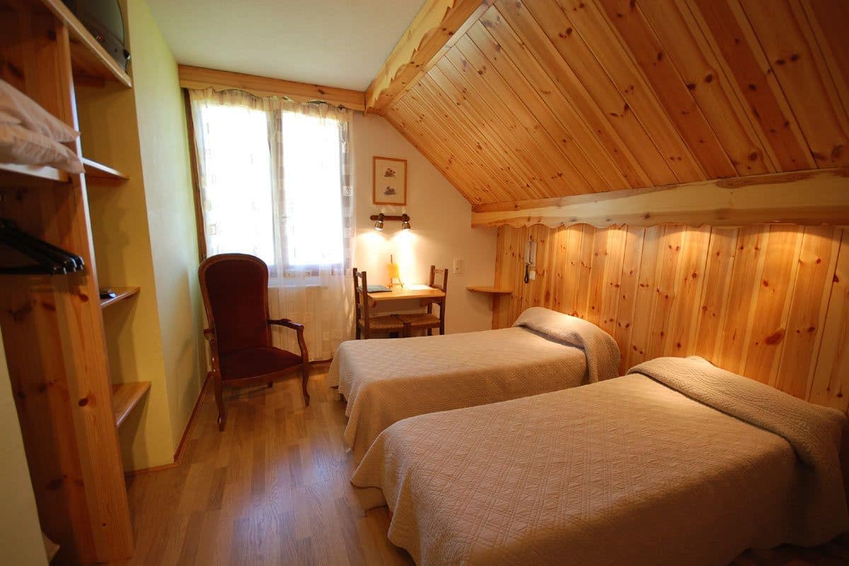 Una habitación acogedora con dos camas, paredes de madera, una silla y una mesa.
