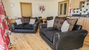 A living room with two black leather sofas, a wooden floor, a dining area, and a kitchen with wooden cabinets. - Mill View (Alnwick)