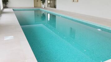 A large indoor swimming pool with clear blue water, tiled walls, and a tiled floor.