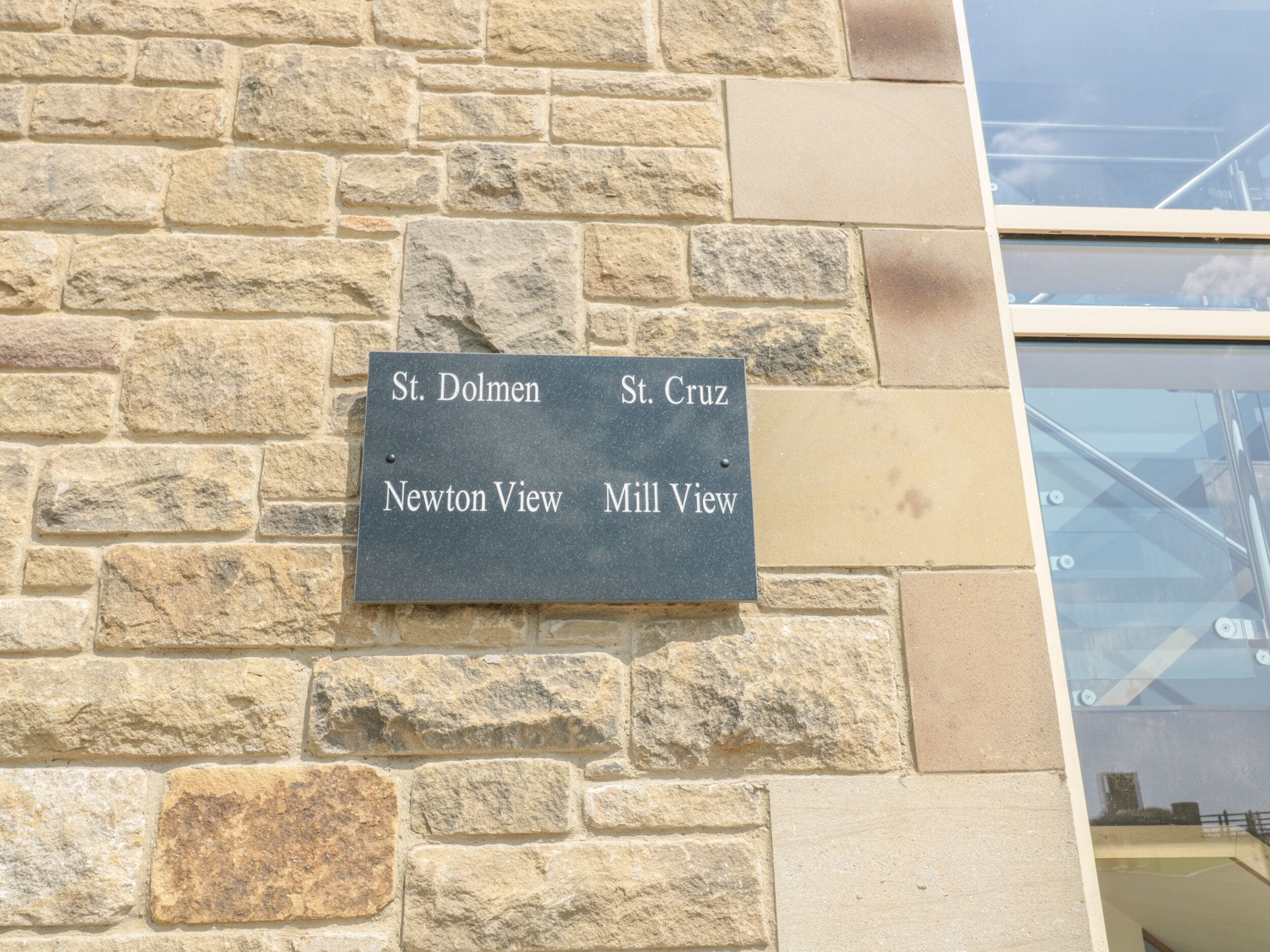 A stone wall with a sign listing names of locations: St. Dolmen, St. Cruz, Newton View, Mill View.