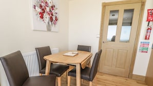 A dining area with a wooden table and four chairs, a radiator, a fire safety sign, and a door with a glass panel. - Mill View (Alnwick)