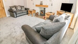 A cozy living room with a fireplace, a sofa, a television, and a painting on the wall. - Croft Cottage (Skipton)