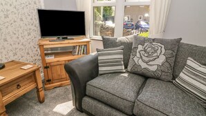 A living room with a grey sofa, a wooden TV stand, and a bookshelf. - Croft Cottage (Skipton)