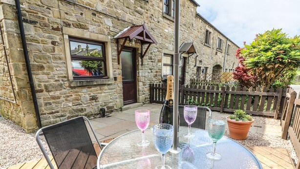 An outdoor seating area with a round glass table, metal chairs, and a bottle of champagne. - Croft Cottage (Skipton)