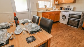 A well-lit kitchen with wooden cabinets, a built-in oven, and a washing machine. - Croft Cottage (Skipton)