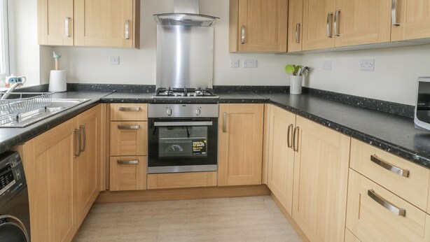 A modern kitchen with wooden cabinets, a stainless steel range hood, a built-in oven, and a black countertop. - Bedlinog (Amlwch)