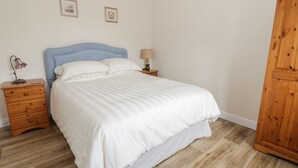 A bedroom with a bed, wooden nightstand, lamp, and wardrobe. - Bedlinog (Amlwch)