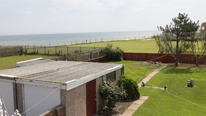 En bostadsfastighet med utsikt över havet, en inhägnad trädgård och en liten byggnad med ett platt tak.