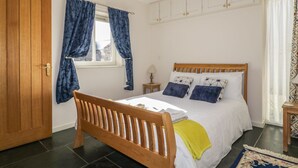 Un dormitorio con cama de madera, ropa de cama blanca, una ventana con cortinas azules y una alfombra estampada.